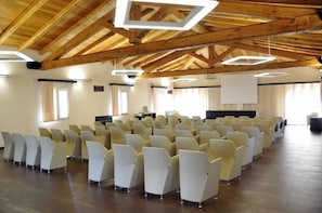 A conference room with rows of chairs, wooden beams on the ceiling, and large windows. - Tenuta Pilastru (Arzachena)