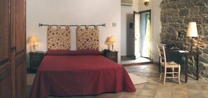 A bedroom with a large bed, two nightstands with lamps, a wooden chair, and a stone wall. - Tenuta Pilastru (Arzachena)