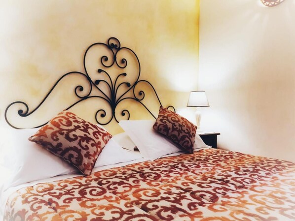 A bed with a patterned bedspread, two patterned pillows, a decorative headboard, and a bedside lamp. - Tenuta Pilastru (Arzachena)