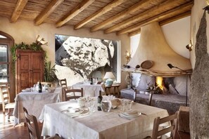 A dining area with wooden tables and chairs, a stone wall, and a fireplace. - Tenuta Pilastru (Arzachena)