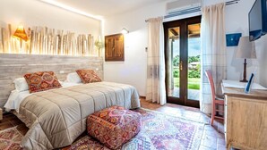 A bedroom with a bed, a wooden headboard, a patterned rug, a desk, and a TV. - Tenuta Pilastru (Arzachena)