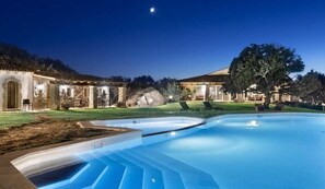A swimming pool with a stone structure and a tree in the background. - Tenuta Pilastru (Arzachena)