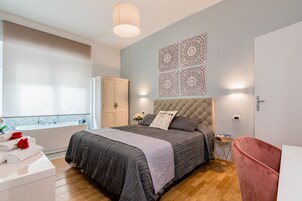 Un dormitorio con cama, tocador, silla y ventana.