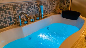 A bathtub with blue water, a modern faucet, and a mosaic tile wall. - Fior di Loto Rooms (Cagliari)