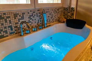 Una bañera con agua azul, un grifo moderno y una pared de mosaicos.