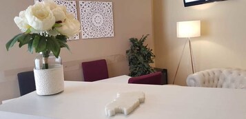 Una mesa de conferencias con mantel blanco, un florero con flores blancas y un adorno blanco.
