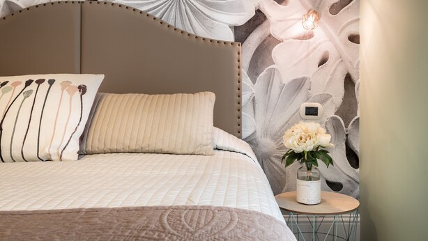 A bedroom with a bed, pillows, a nightstand with a vase of flowers, and a wall with a floral mural. - Fior di Loto Rooms (Cagliari)
