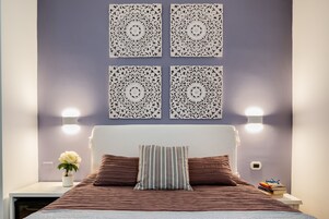 Un dormitorio ordenado con cama, almohadas, mesita de noche con lámpara y aplique de pared.