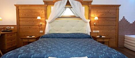 Un dormitorio con una cama grande, cabecera de madera, dos mesitas de noche con lámparas y una ventana con cortinas.