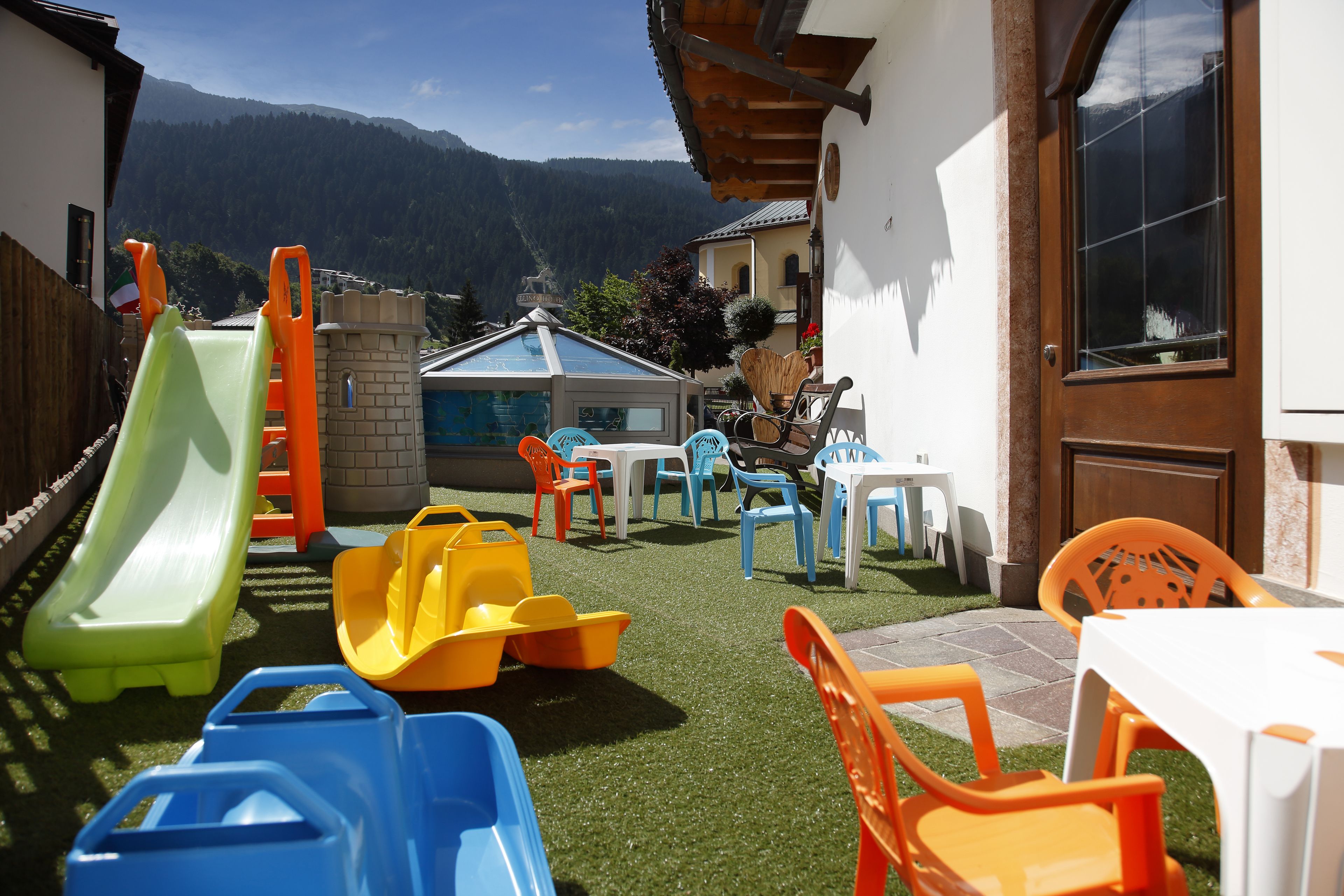 Area giochi per bambini con scivoli e arredi in plastica, con montagne sullo sfondo.