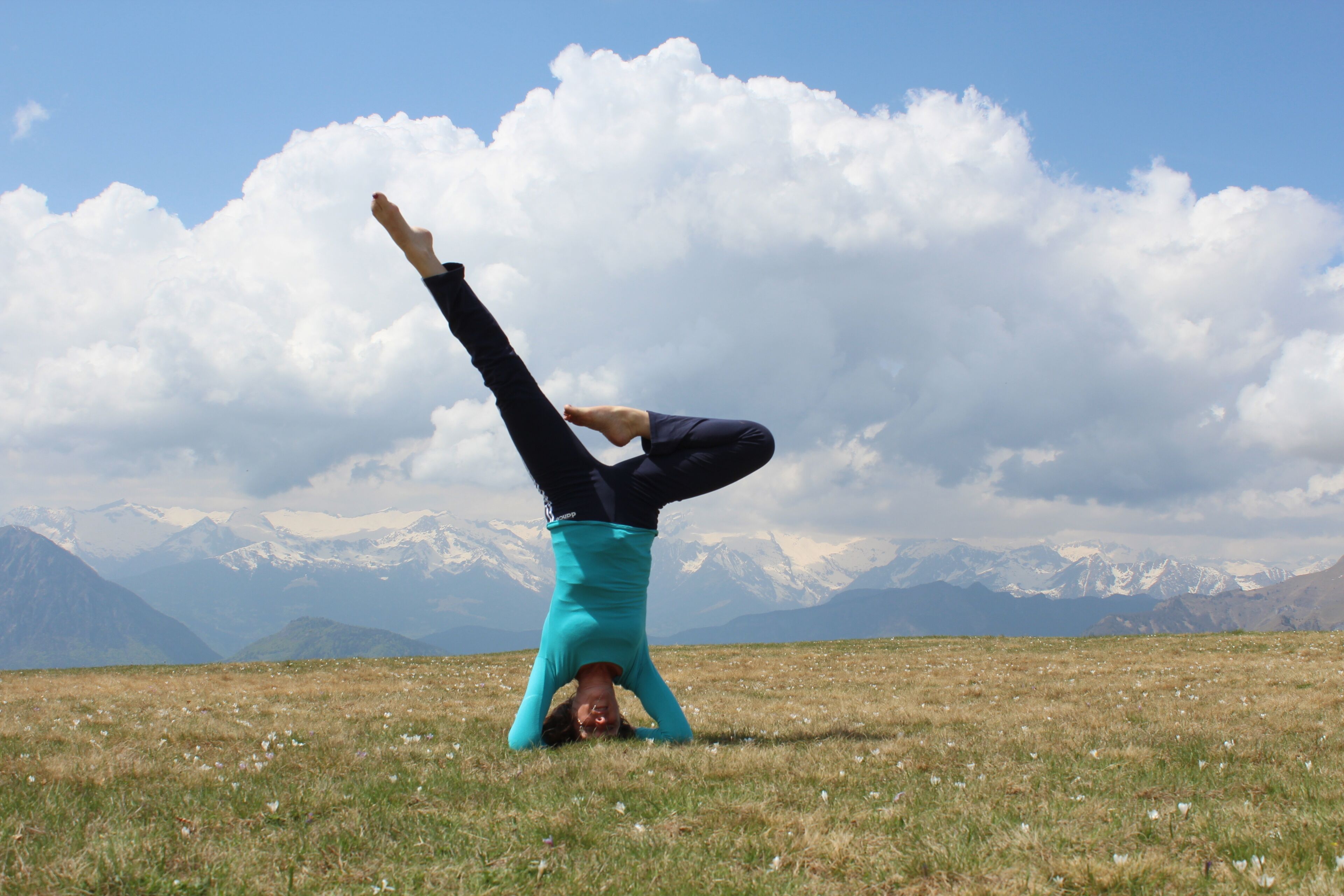 Eine Person macht eine Handstandvorstellung in einem weitläufigen Feld mit Bergen im Hintergrund.