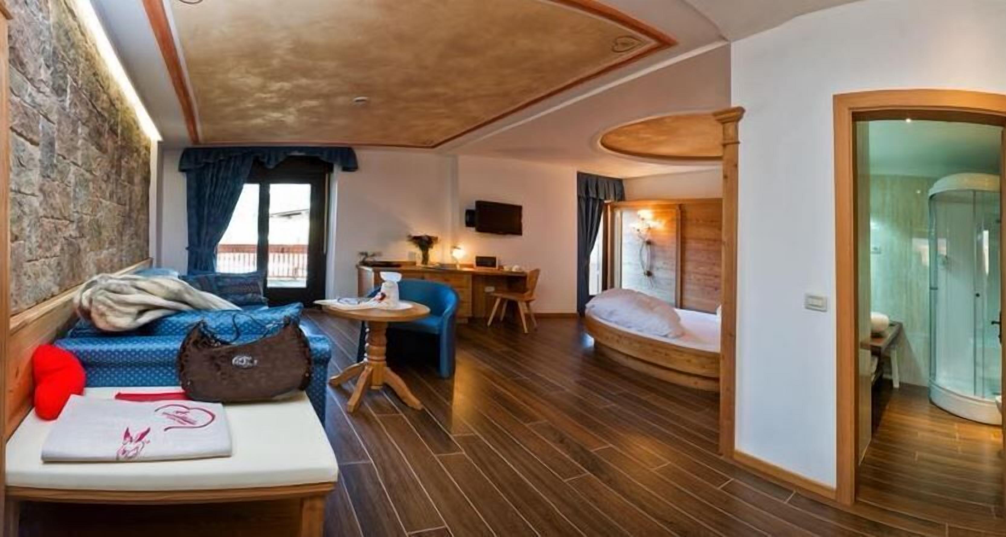 A compact room with a bed, a seating area with a table, a small desk, and a shower area.