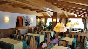 Un restaurante con vigas de madera, manteles verdes y amarillos, y lámparas colgantes.