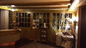 Un área de recepción cálidamente iluminada, con un mostrador de madera, una exhibición de postales en la pared y una planta decorativa.