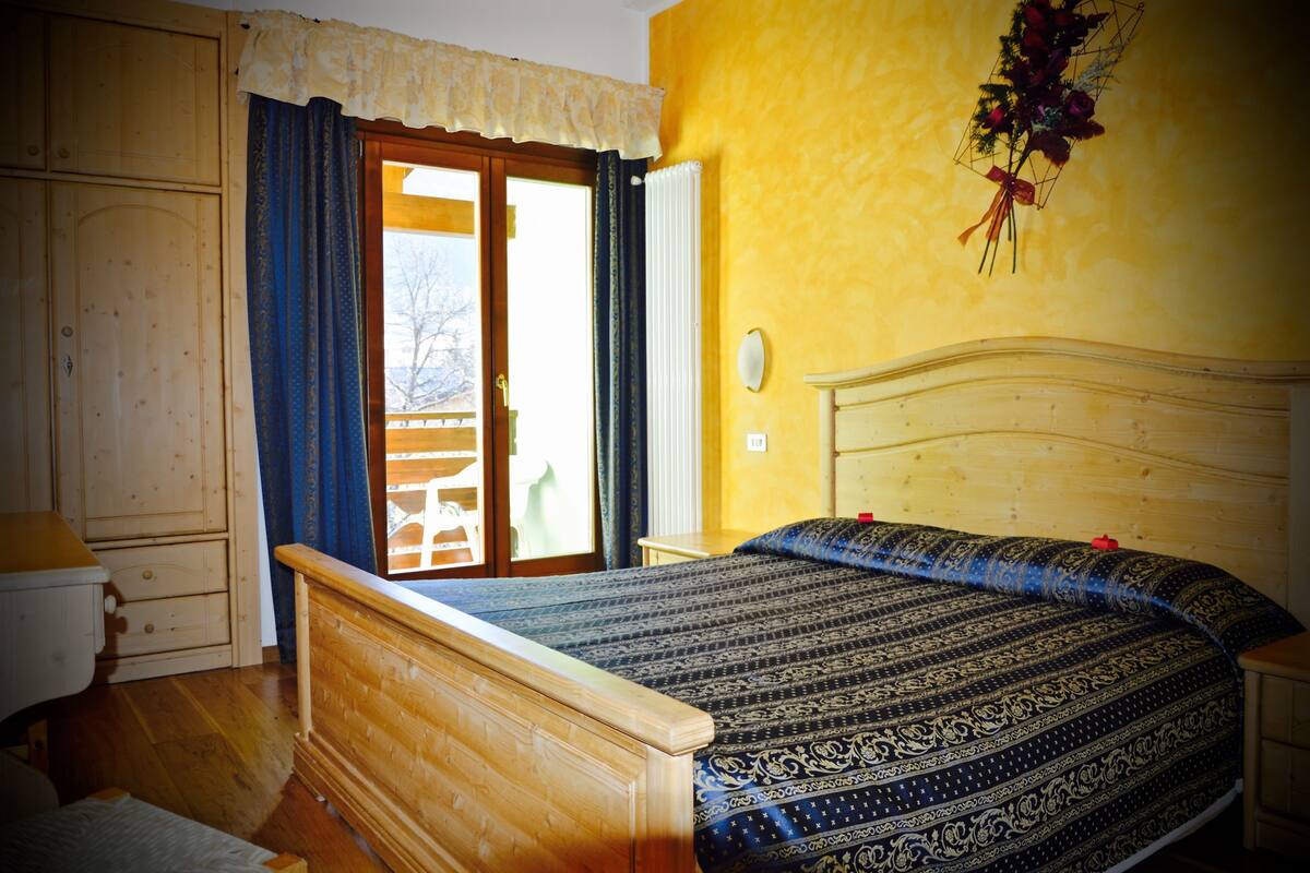 A bedroom with a wooden bed, a nightstand, a dresser, and a window with curtains.