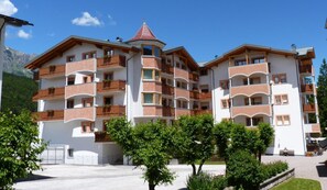 A multi-story hotel with balconies, a red-tiled roof, and a mountainous backdrop.
