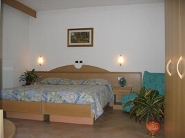 A bedroom with a wooden bed, two bedside tables, a nightstand, a framed picture on the wall, and two wall-mounted lights.