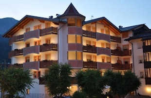 Un hotel de varios pisos con balcones, una torre central y montañas al fondo.