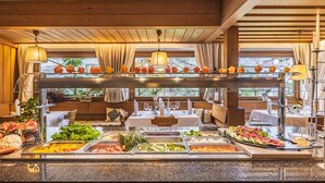 A buffet setup with various food items and a seating area with tables and chairs. - Hotel Erna (Brennero)