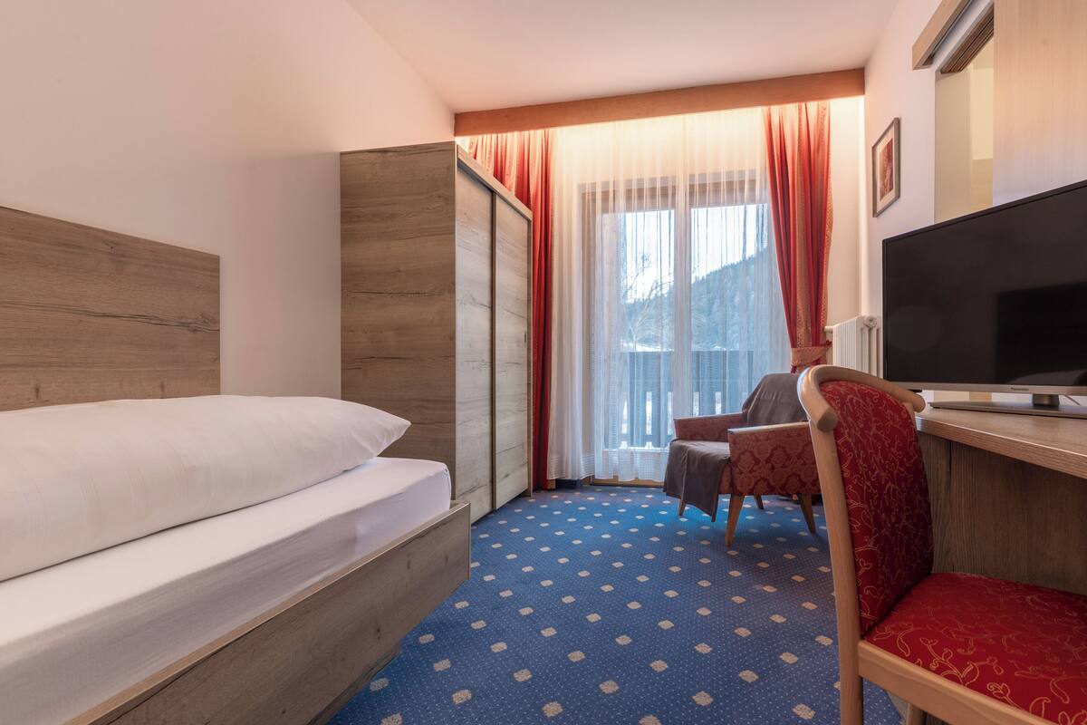 Een hotelkamer met een bed, een bureau met een televisie, een stoel en een raam met gordijnen.