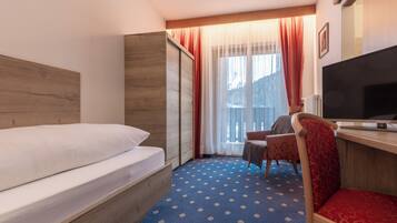 Una camera d'albergo con un letto, una scrivania con televisore, una sedia e una finestra con tende.