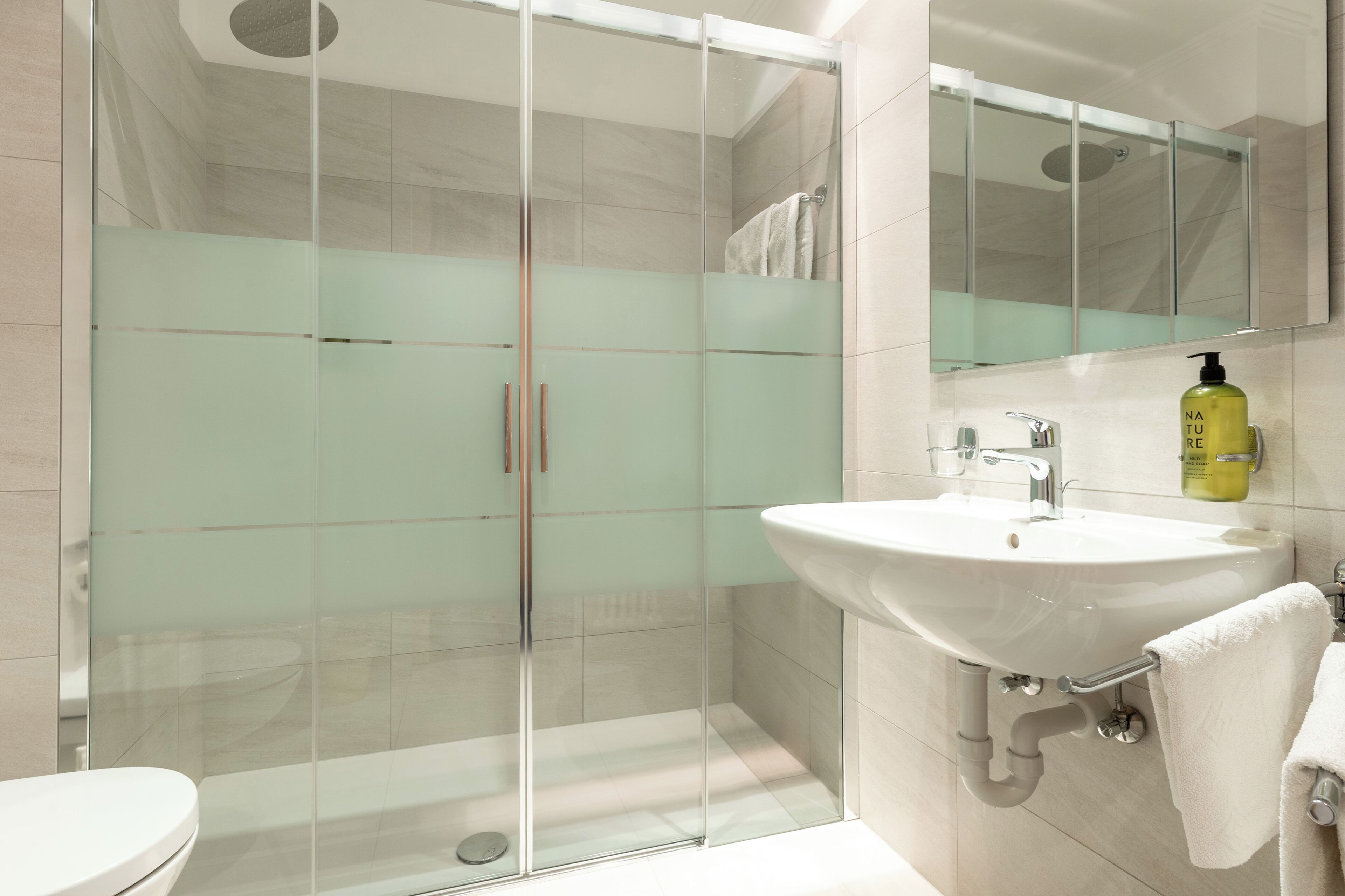 Ein modernes Badezimmer mit einer Duschkabine, einem weißen Waschbecken und einem Spiegel darüber.