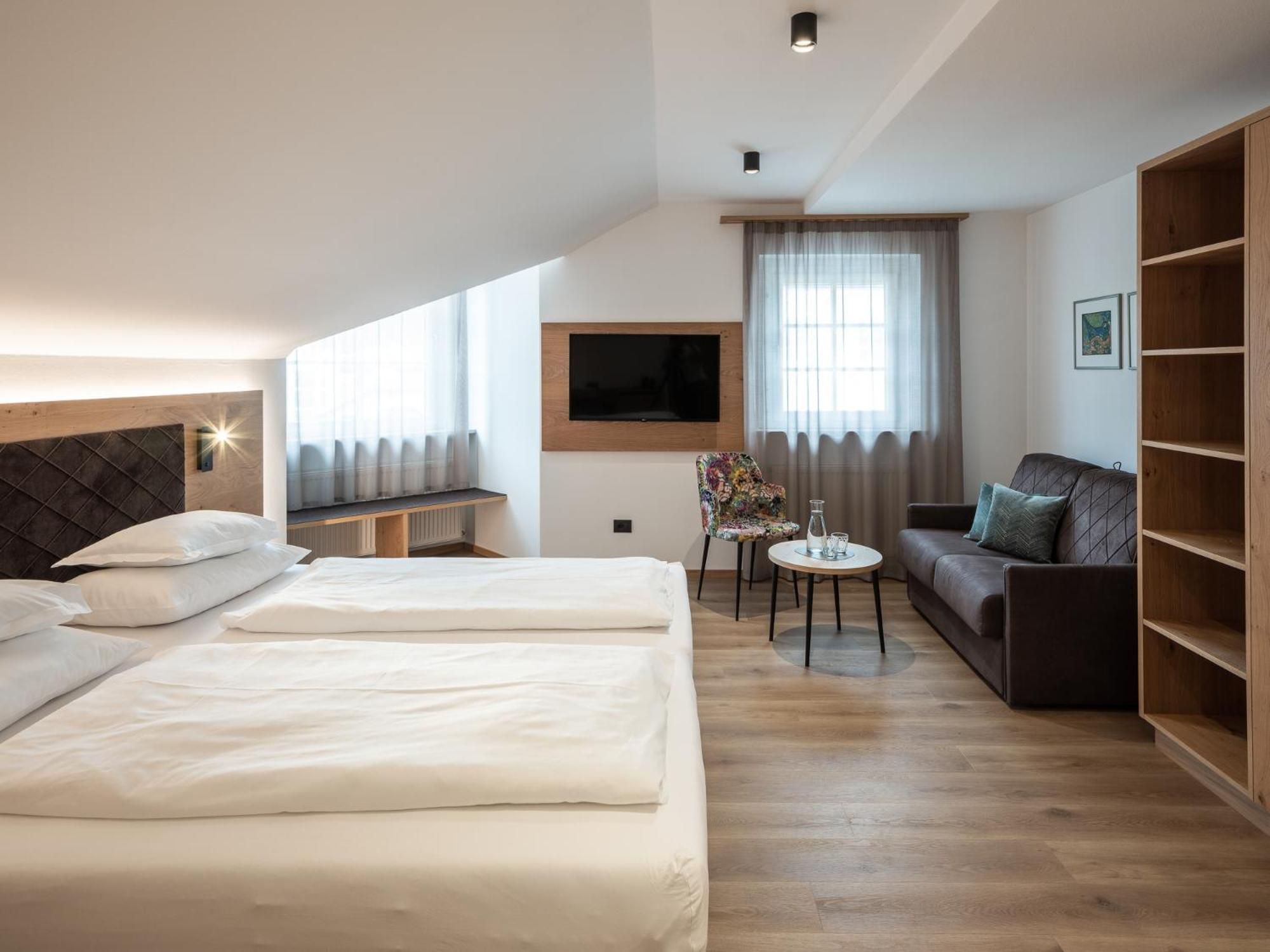 A hotel room with two beds, a sofa, a small table, a TV, and a bookshelf.