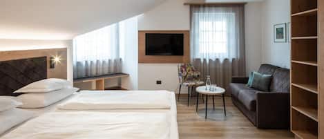 A hotel room with two beds, a sofa, a small table, a TV, and a bookshelf.