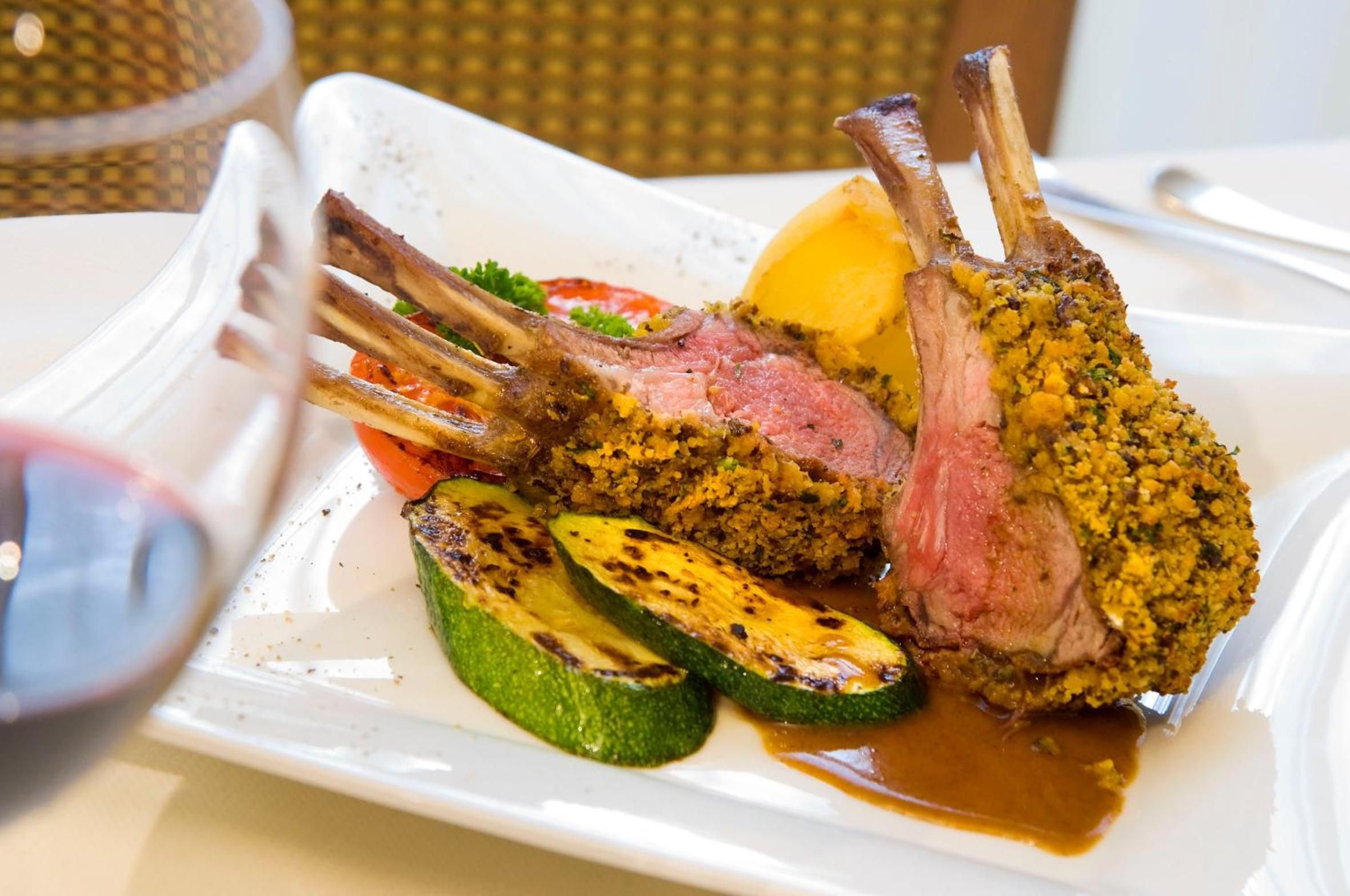 Un piatto con costolette di agnello, verdure grigliate e salsa.