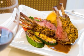 A plate with a lamb rack, grilled vegetables, and a sauce.