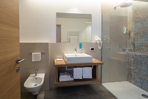 A modern bathroom with a bidet, a sink, a mirror, and a shower.