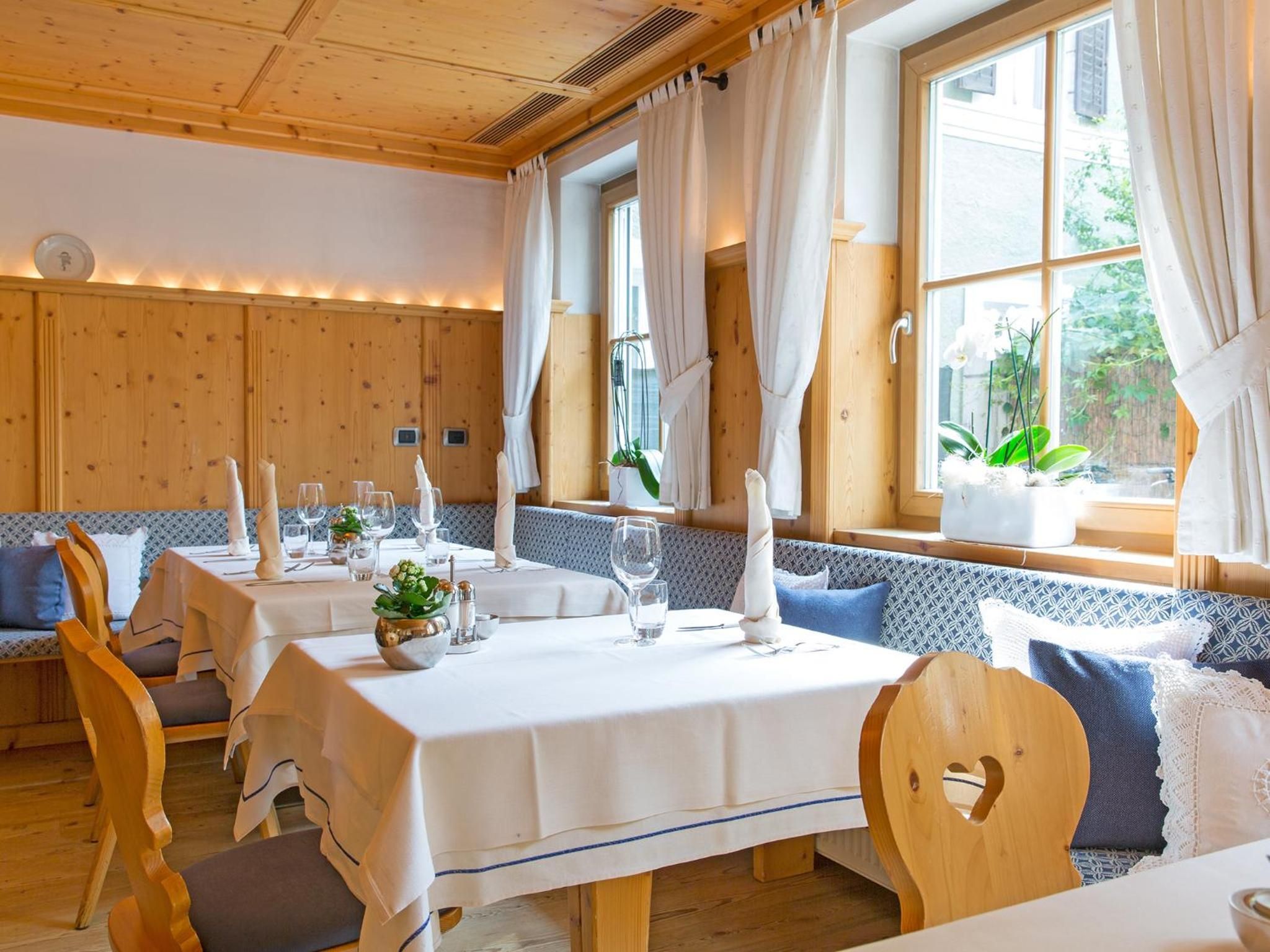 A dining area with wooden tables and benches, white tablecloths, and natural light from large windows.