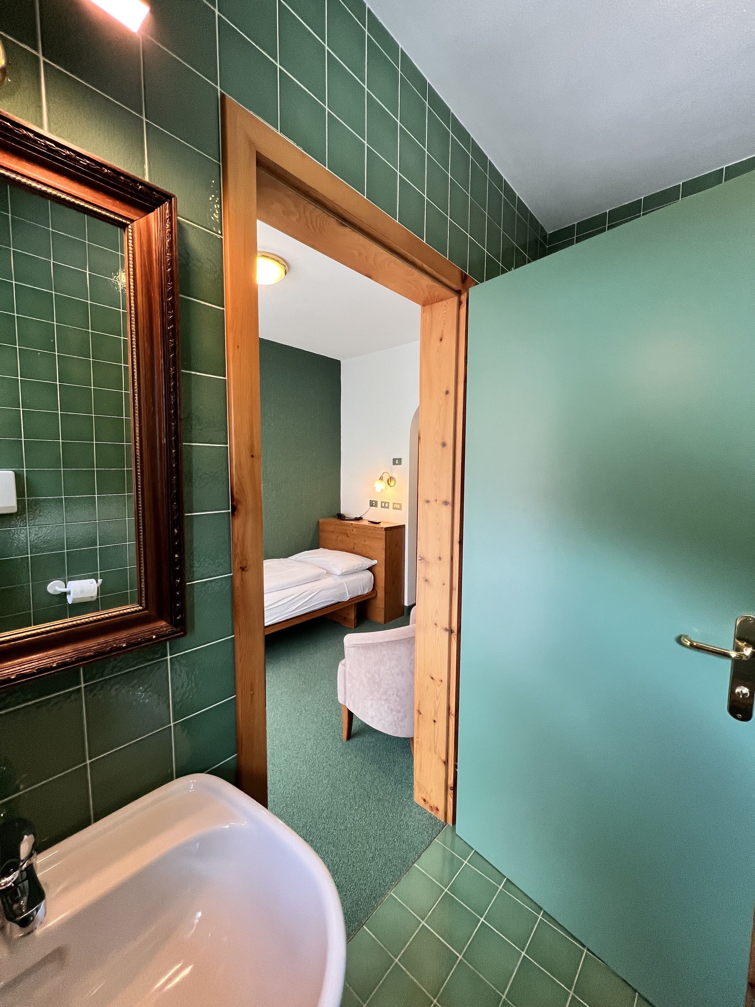 A bathroom with a sink, mirror, and green tiled walls.