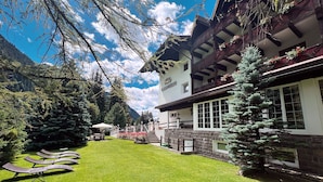 Um hotel com um jardim bem cuidado, área de estar externa e montanhas ao fundo.