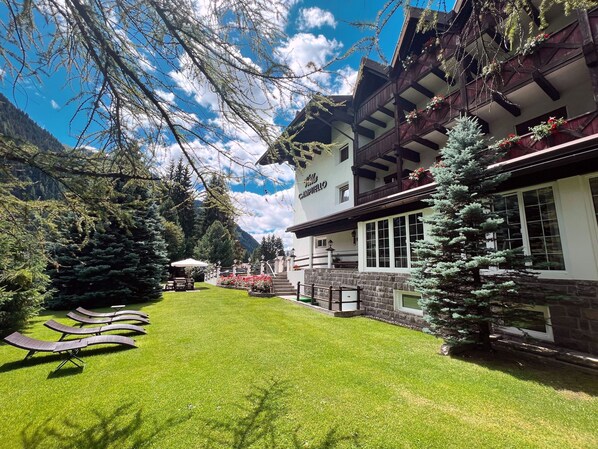 A hotel with a well-maintained lawn, outdoor seating, and a mountainous backdrop. - B&B Garni Villa Campitello (Campitello di Fassa)