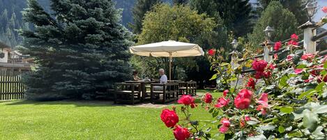 Eine Terrasse mit Holztischen und -stühlen, umgeben von einem gepflegten Rasen und roten Rosen.