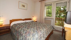 A bedroom with a bed, bedside lamps, a window with a view, and a television. - Villa Rosa (Campitello di Fassa)
