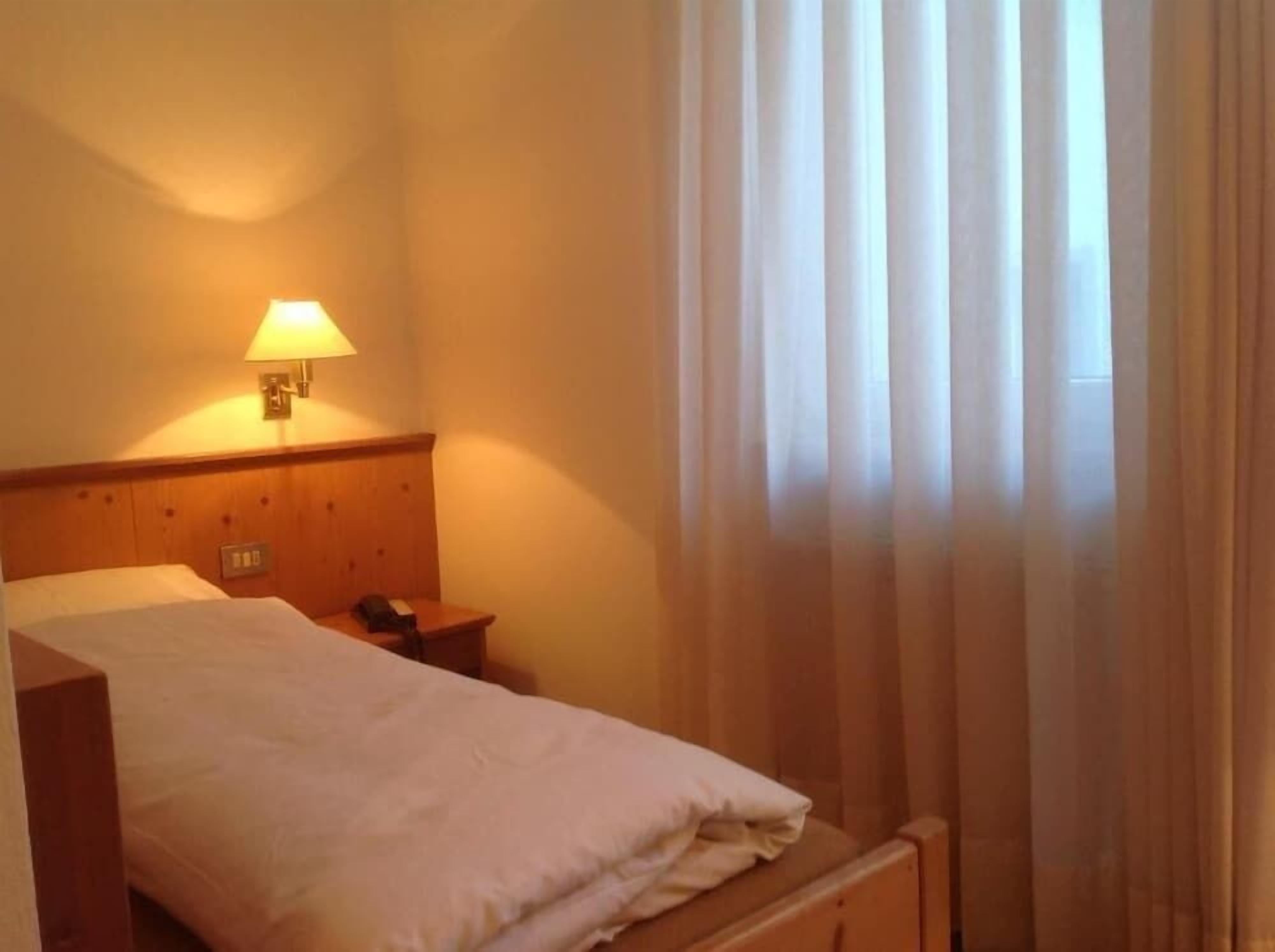 A hotel room with a bed, a bedside table, a lamp, and a window with curtains.