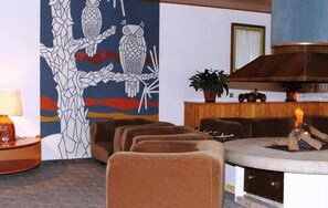 Una habitación con chimenea, un mural en la pared con lechuzas y una zona de estar con sillones marrones.