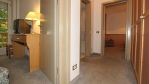 A room with a desk, a lamp, a television, and a door leading to another room. - Villa Rosa (Campitello di Fassa)