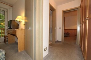 A room with a desk, a lamp, a television, and a door leading to another room. - Villa Rosa (Campitello di Fassa)