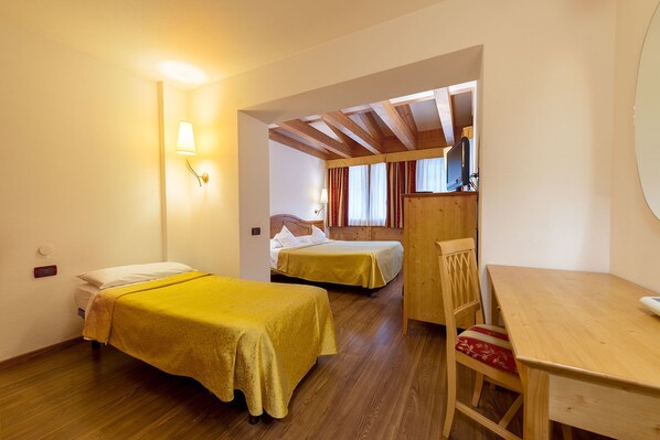 A room with two beds, a wooden table, and a television. - Alpino Al Cavalletto (Canazei)