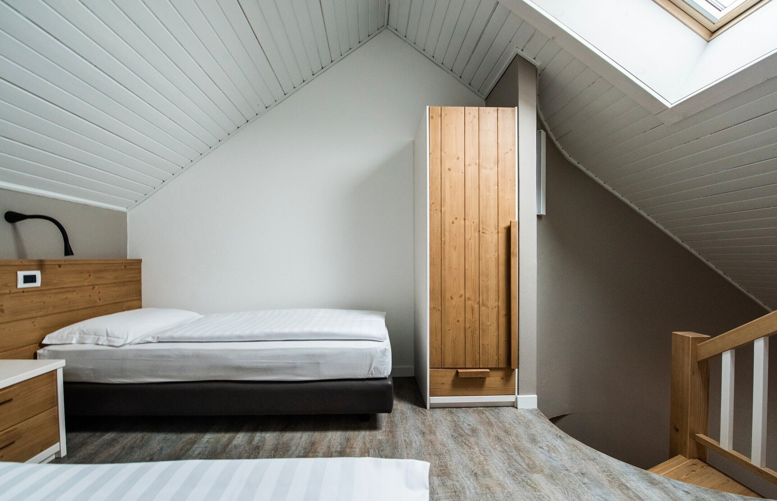 A bedroom with a sloped ceiling, a bed, a wooden wardrobe, and a skylight.