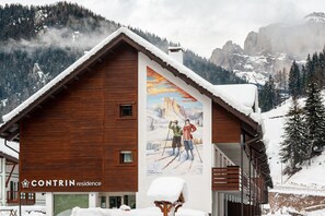 A wooden cabin with a ski-themed mural, a wooden exterior, and a snowy mountain backdrop.
