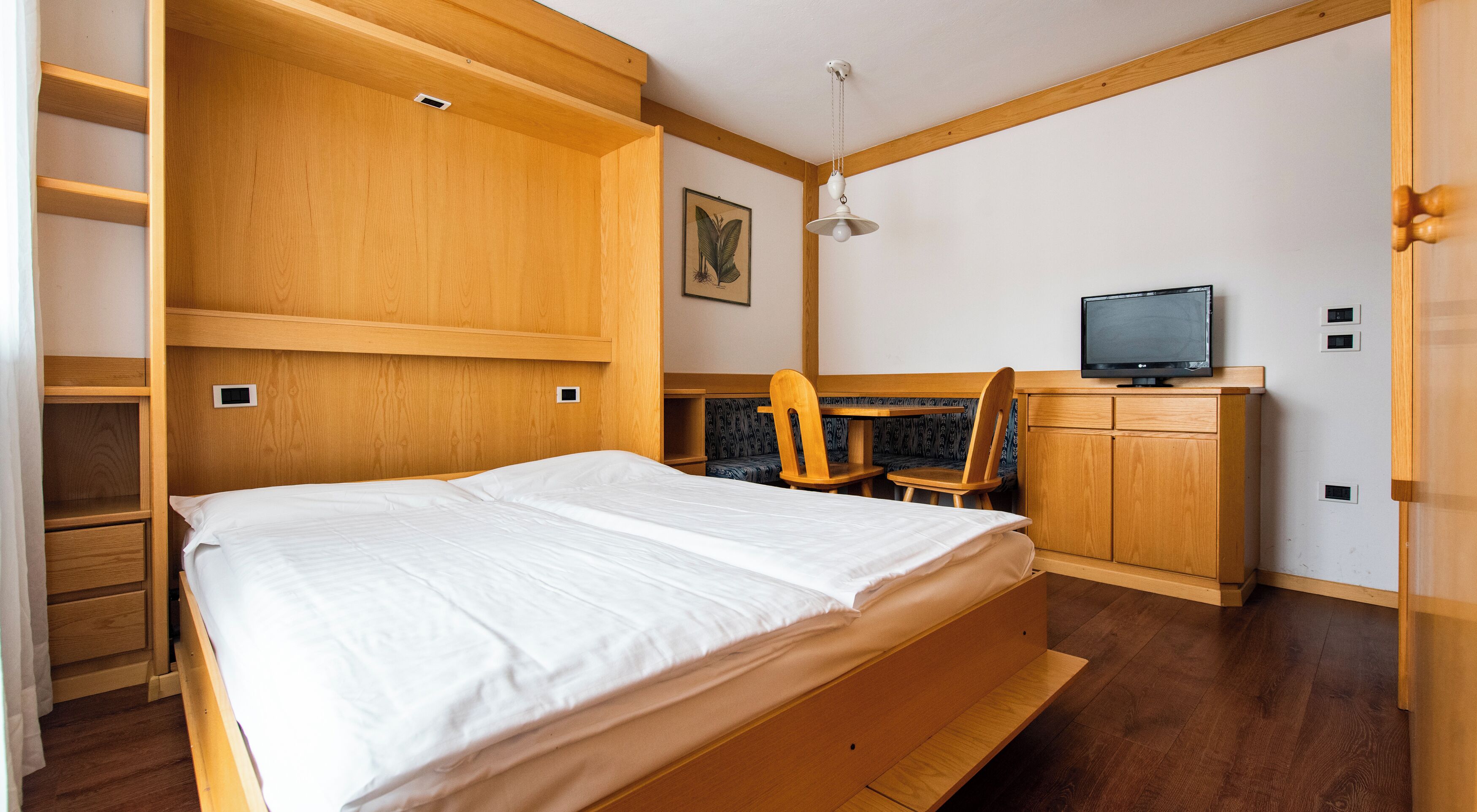 A wooden bunk bed with a TV and seating area in a room with white walls and wooden floors.
