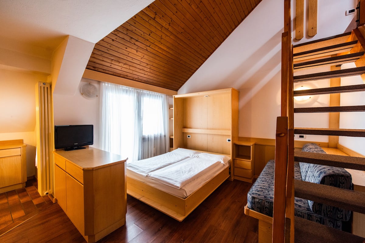 A compact room with a bunk bed, a desk, and a television.