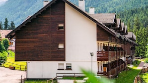 Eine Holzhütte mit Balkon, vor einer Bergkulisse und blauem Himmel.