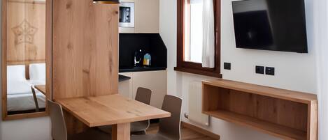 Una habitación de hotel moderna con una mesa de comedor de madera, dos sillas, un televisor montado en la pared y un espejo grande.