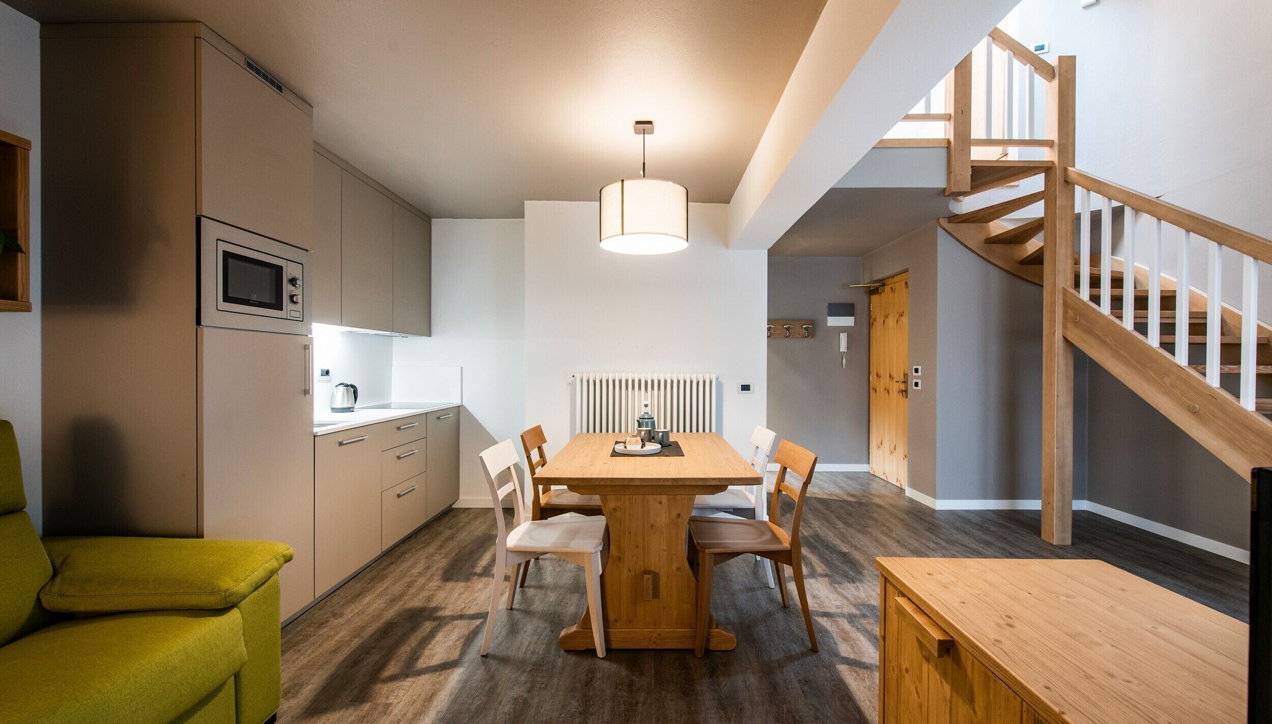 A modern kitchen with a dining table, chairs, and a staircase.