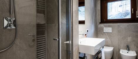 Une salle de bain moderne dotée d’une douche à parois de verre, d’un meuble-lavabo avec bidet et d’une grande fenêtre au-dessus du lavabo.